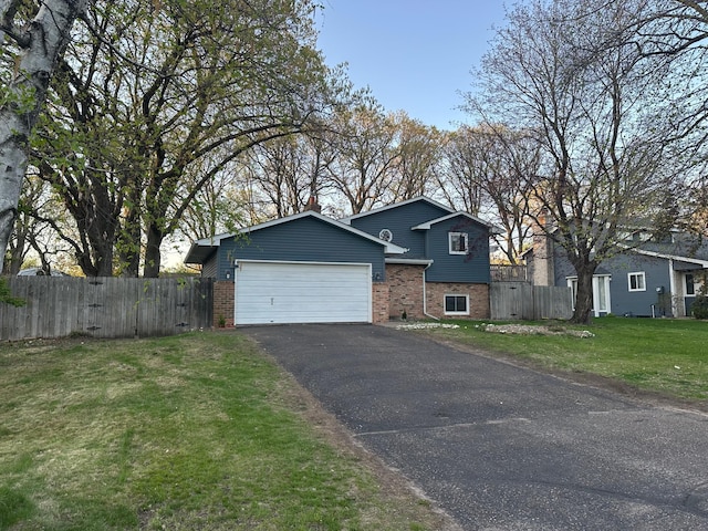 split level home with aphalt driveway, fence, a garage, and brick siding