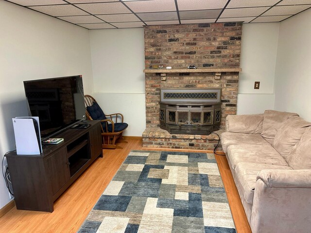 living room with light wood-type flooring, a fireplace, a paneled ceiling, and baseboards