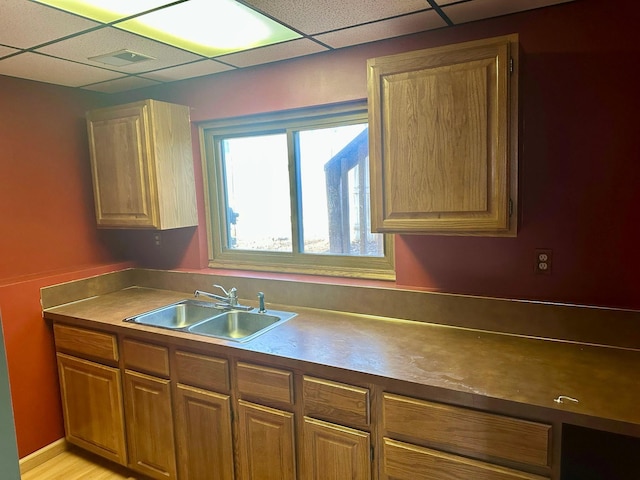kitchen with a sink, a drop ceiling, and brown cabinetry