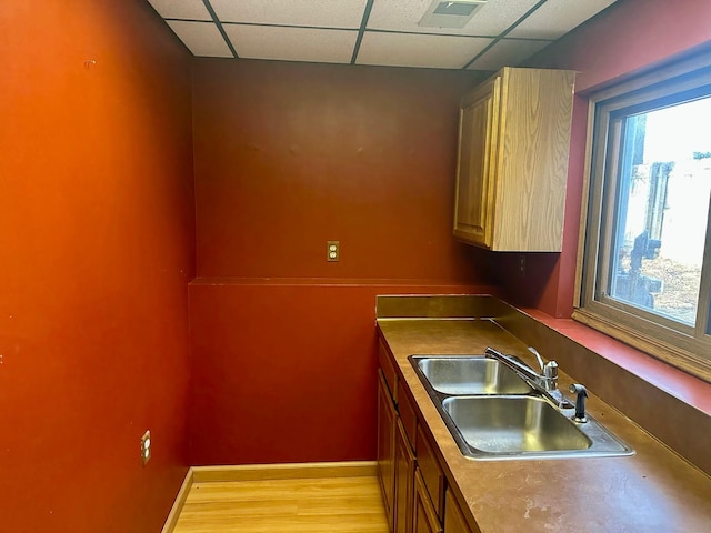 kitchen with a sink, a paneled ceiling, and baseboards