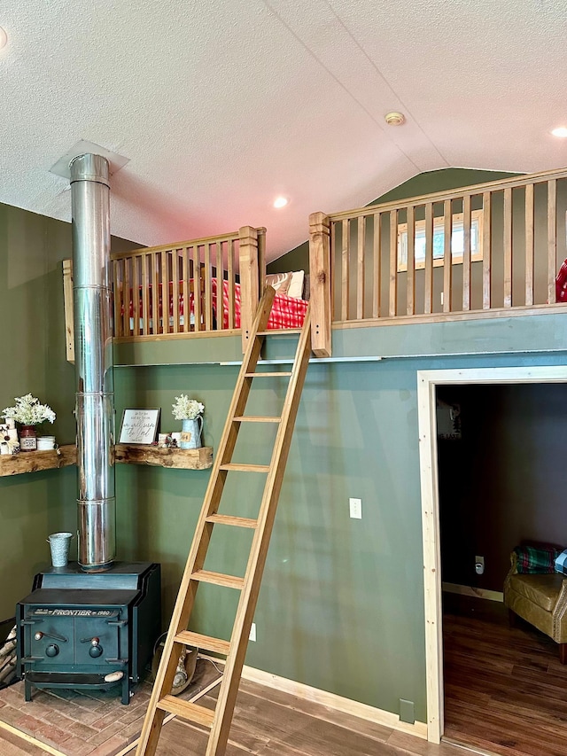 38985 337th Ln, Aitkin, MN 56431 - bedroom featuring vaulted ceiling, wood finished floors, a wood stove, baseboards, and a textured ceiling