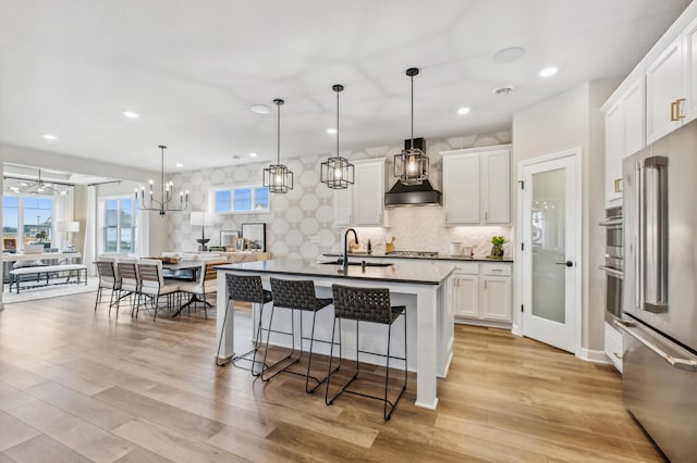 1331 150th St W, Rosemount, MN 55068 - kitchen with dark countertops, a sink, light wood-style floors, stainless steel appliances, and wall chimney exhaust hood