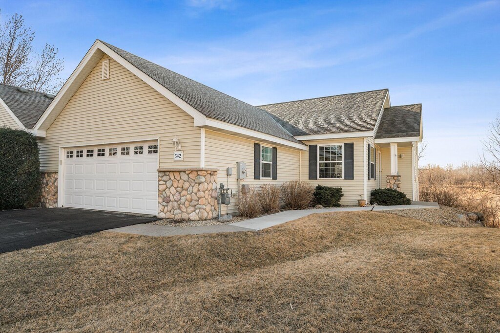 view of front of home with driveway, stone siding, a garage, and roof with shingles