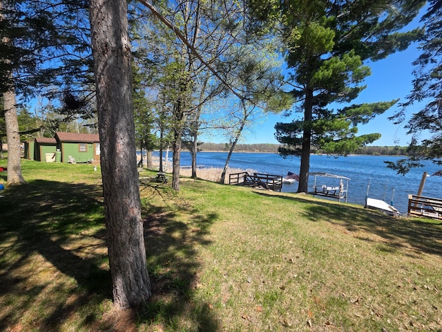 view of grassy yard with a water view and a dock