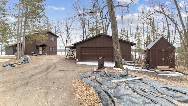 view of snowy exterior with an outdoor structure, a garage, and asphalt driveway