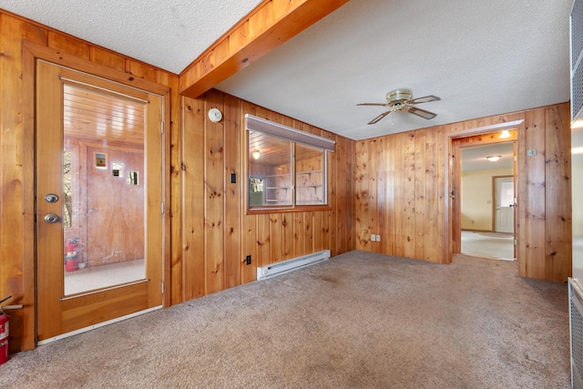 carpeted spare room featuring baseboard heating, a textured ceiling, wooden walls, and a ceiling fan