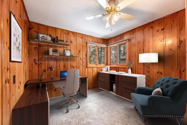 office space featuring light colored carpet, a textured ceiling, ceiling fan, and wood walls