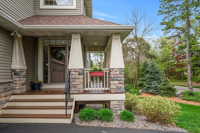 doorway to property featuring a shingled roof, stone siding, and covered porch