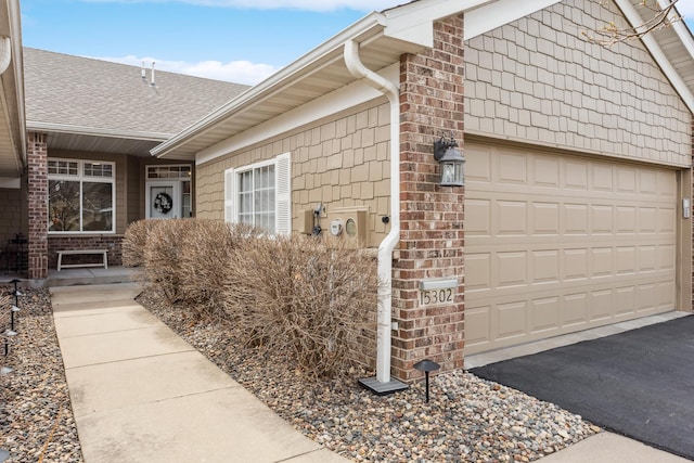view of home's exterior featuring driveway, a shingled roof, an attached garage, and brick siding