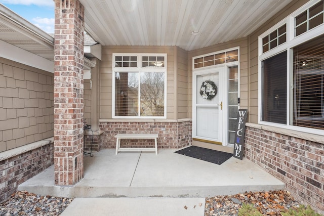 entrance to property featuring a porch and brick siding