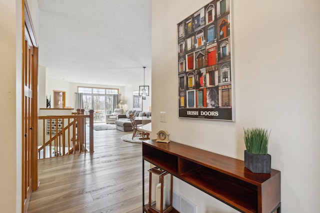 corridor featuring an upstairs landing, wood finished floors, and a chandelier