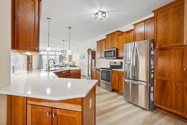 kitchen featuring appliances with stainless steel finishes, a sink, a peninsula, brown cabinets, and a textured ceiling