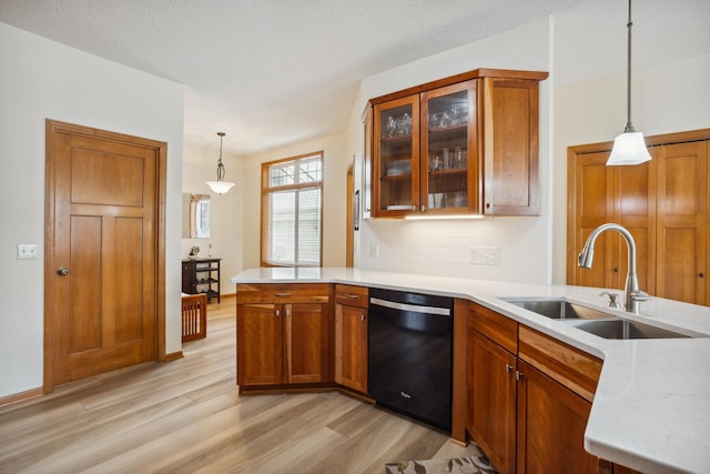 kitchen with dishwasher, a peninsula, a sink, light wood-style flooring, and brown cabinetry