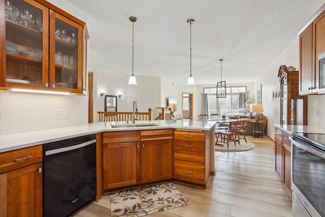 kitchen with appliances with stainless steel finishes, a peninsula, a sink, light wood-style flooring, and light countertops
