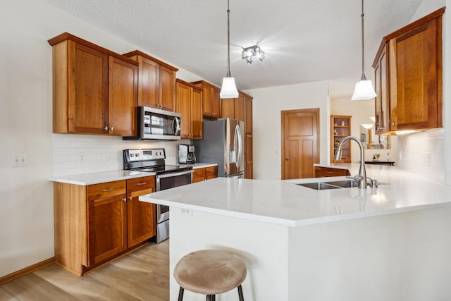 kitchen featuring appliances with stainless steel finishes, a sink, light wood-type flooring, tasteful backsplash, and a peninsula