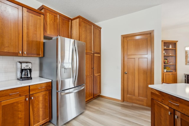 kitchen featuring stainless steel refrigerator with ice dispenser, brown cabinetry, light wood-style flooring, decorative backsplash, and light countertops