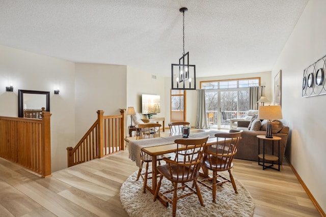dining space featuring light wood finished floors, a textured ceiling, a chandelier, and baseboards