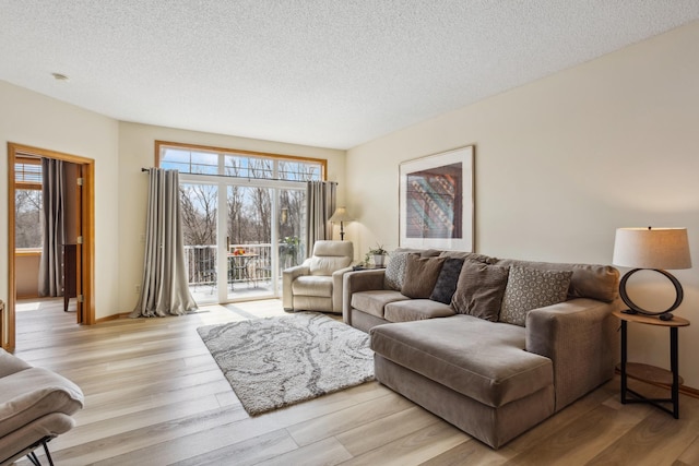 living room with light wood-type flooring, a textured ceiling, and baseboards
