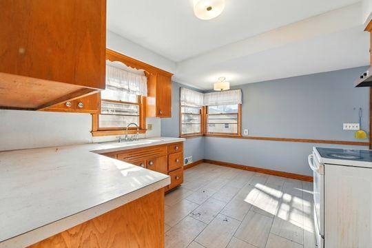 7335 Penn Ave S, Richfield, MN 55423 - kitchen with baseboards, light countertops, brown cabinetry, white electric range oven, and a sink