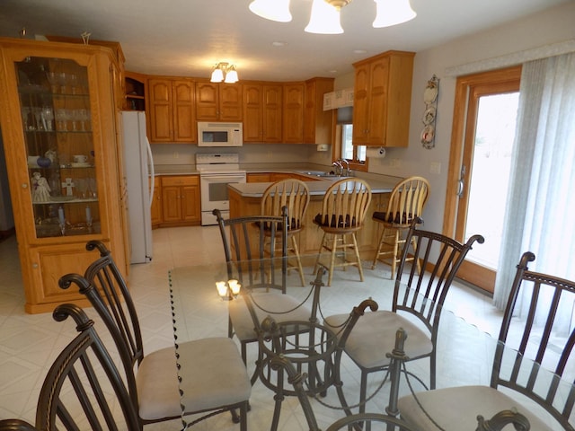 kitchen featuring a sink, white appliances, a kitchen bar, a peninsula, and light floors
