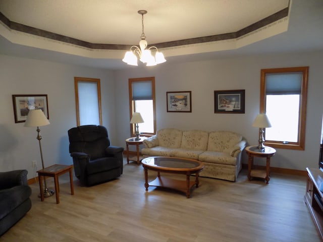 living room with a raised ceiling, light wood-style floors, a chandelier, and a healthy amount of sunlight