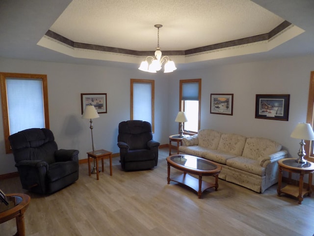 living area with baseboards, a raised ceiling, an inviting chandelier, a textured ceiling, and light wood finished floors
