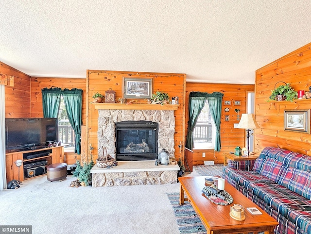 living area featuring a textured ceiling, carpet flooring, wooden walls, and a stone fireplace
