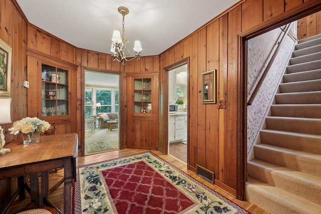 19135 Highland Ave, Deephaven, MN 55391 - entrance foyer with wood walls, a chandelier, light wood finished floors, and stairs
