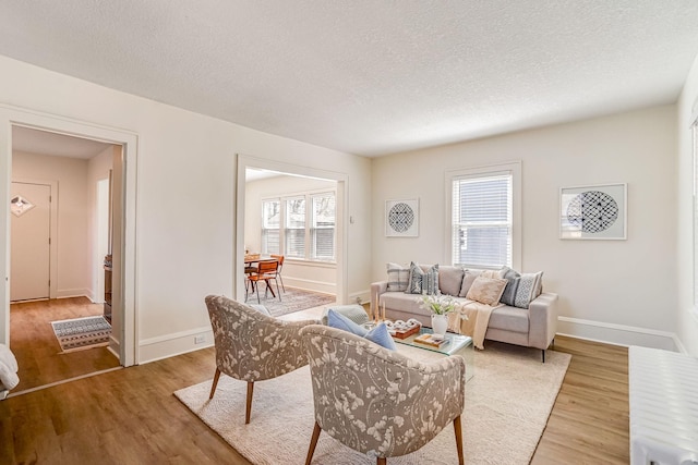 living room with baseboards, a textured ceiling, and light wood-style flooring