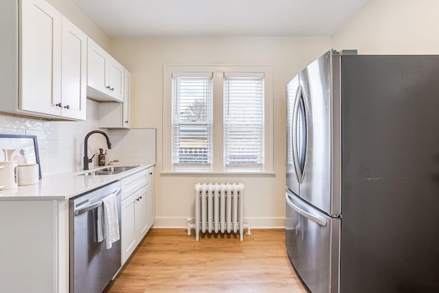 kitchen with baseboards, radiator heating unit, light countertops, a sink, and appliances with stainless steel finishes