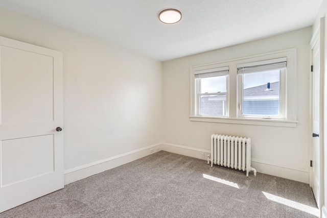 carpeted empty room featuring baseboards and radiator heating unit