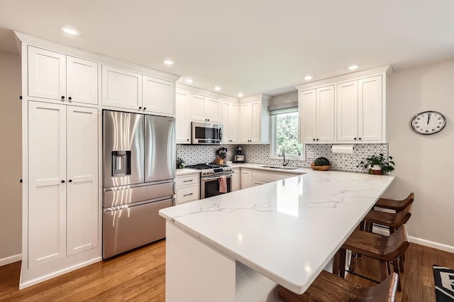 7488 Hydram Ave S, Cottage Grove, MN 55016 - kitchen featuring appliances with stainless steel finishes, a peninsula, light wood-style flooring, a sink, and a kitchen breakfast bar
