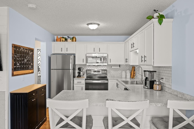 1324 Pembrooke Ln, Waconia, MN 55387 - kitchen featuring appliances with stainless steel finishes, light countertops, a peninsula, white cabinets, and a textured ceiling