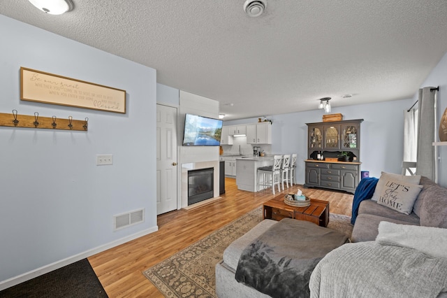 1324 Pembrooke Ln, Waconia, MN 55387 - living area with a textured ceiling, light wood-style flooring, and a glass covered fireplace