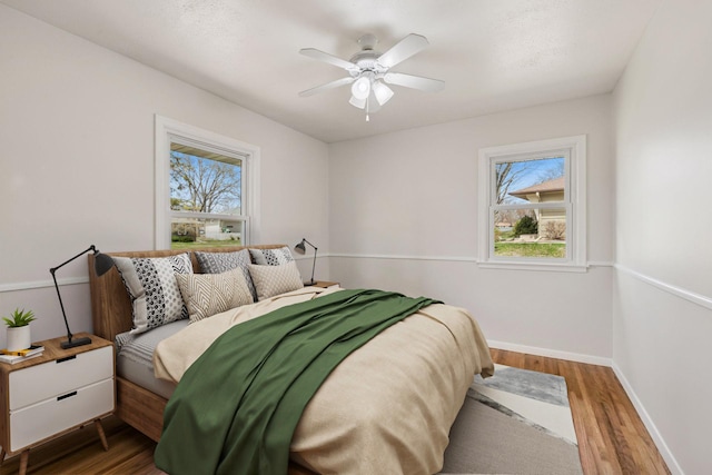 bedroom featuring baseboards, multiple windows, a ceiling fan, and wood finished floors