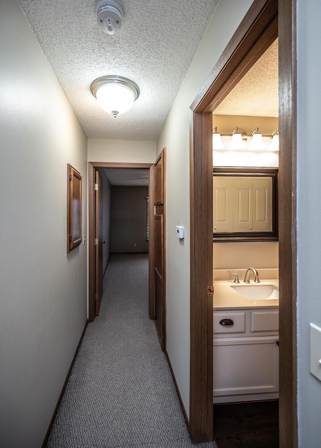 corridor with a textured ceiling, a sink, and carpet floors