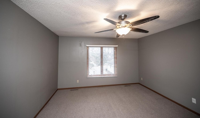 spare room with a ceiling fan, light colored carpet, a textured ceiling, and baseboards