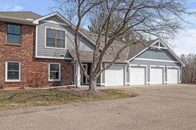 traditional home with board and batten siding, aphalt driveway, roof with shingles, brick siding, and an attached garage