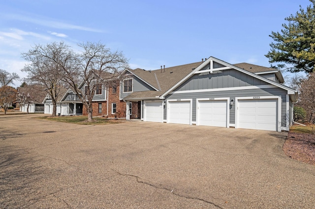 view of front facade featuring an attached garage, board and batten siding, aphalt driveway, and brick siding