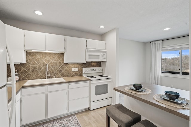 kitchen with white appliances, light wood-style flooring, white cabinetry, backsplash, and a sink