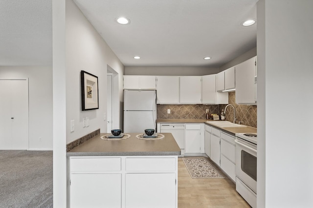 kitchen with tasteful backsplash, white appliances, a peninsula, white cabinets, and a sink