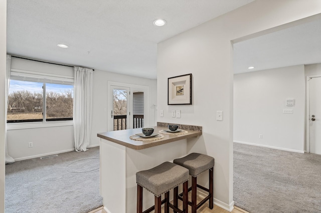 kitchen featuring carpet floors, baseboards, a breakfast bar, and recessed lighting