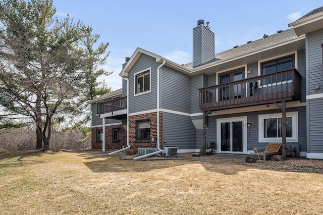 back of property with a balcony, a chimney, cooling unit, brick siding, and a lawn