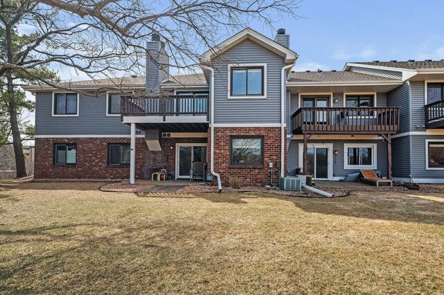 rear view of house featuring a balcony, a chimney, brick siding, and a yard