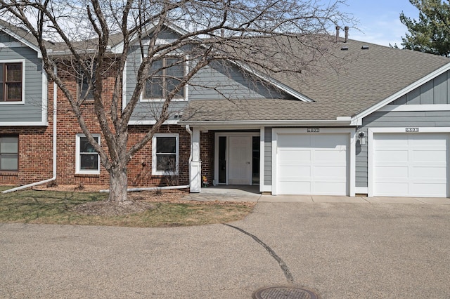 view of front of home featuring brick siding, a shingled roof, a garage, and aphalt driveway