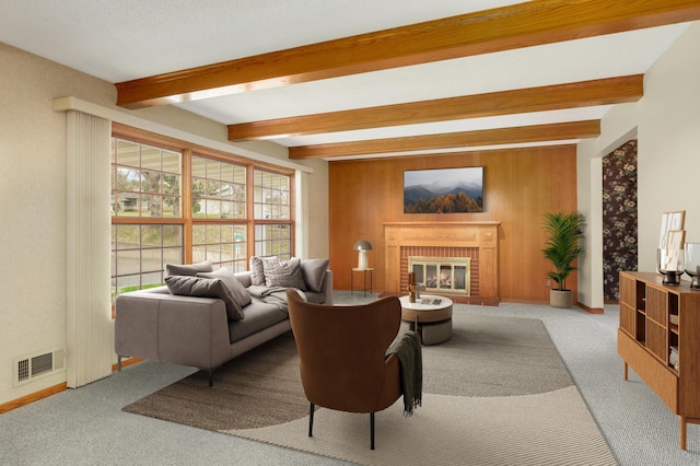carpeted living area featuring beam ceiling, visible vents, a fireplace, wooden walls, and baseboards