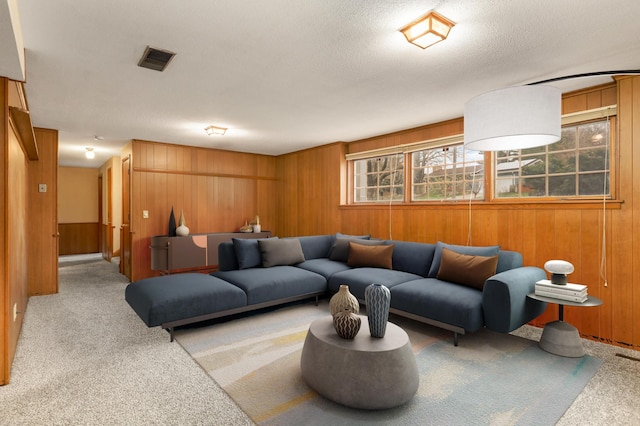 living area featuring light carpet, wooden walls, a textured ceiling, and visible vents