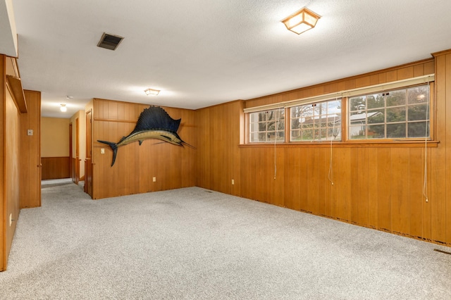 carpeted spare room featuring visible vents and wooden walls