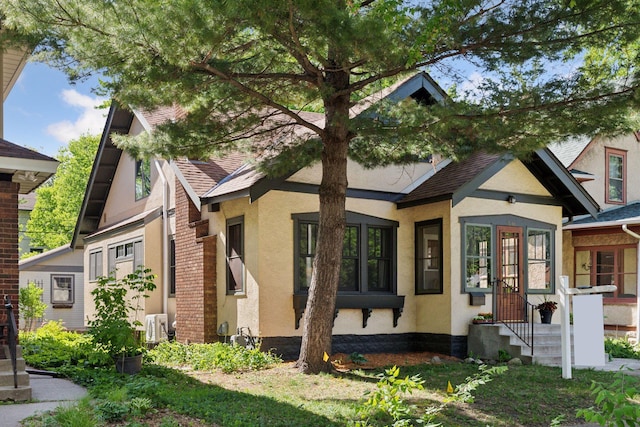 tudor-style house featuring stucco siding, a shingled roof, and ac unit