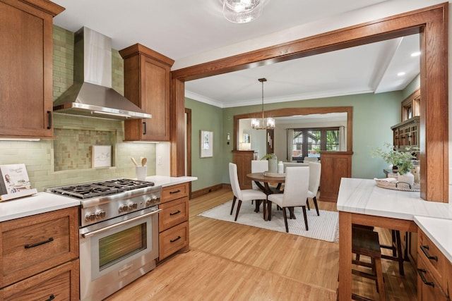 kitchen with wall chimney range hood, high end stainless steel range oven, light wood-type flooring, brown cabinets, and ornamental molding